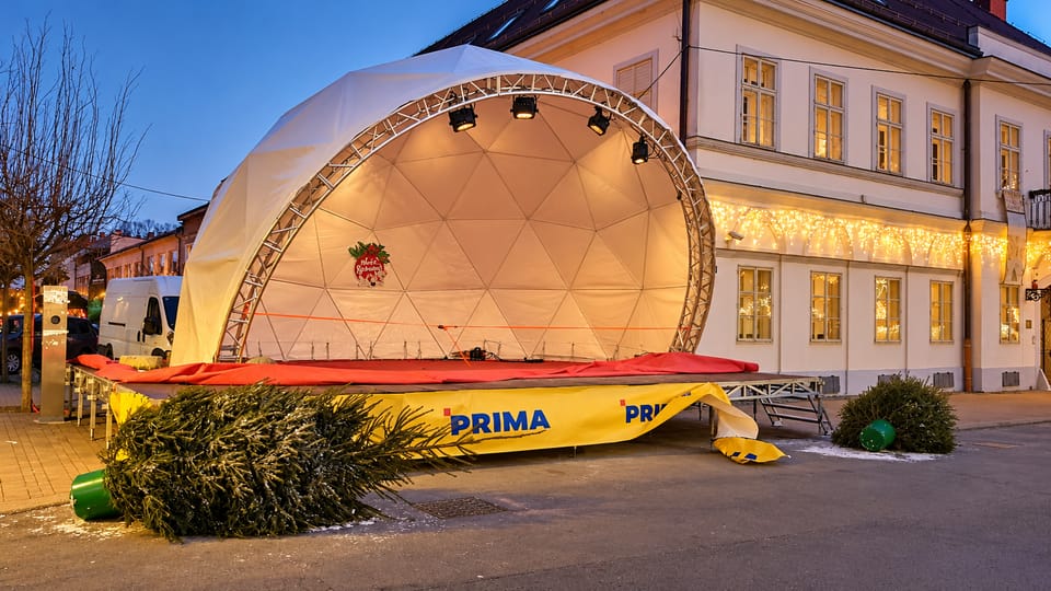 Bijela kupolasta pozornica s truss lukom i reflektorima na gradskom trgu u sumrak, uz blagdanski osvijetljenu zgradu.