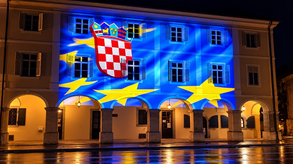 Noćna projekcija hrvatskog grba i žutih zvijezda na plavoj podlozi na pročelju zgrade s arkadama.